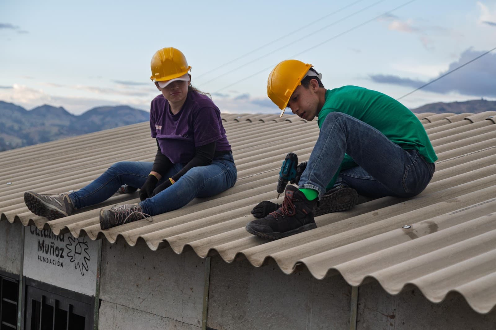 Two volunteers securing a corrugated roof with mountains in the background